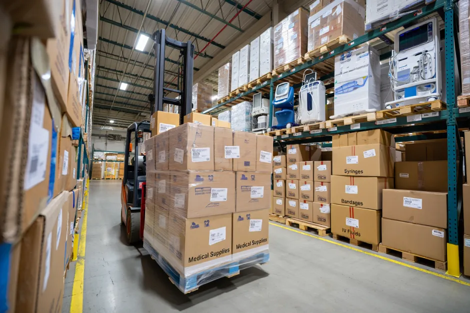 imagine cu un depozit de aparatura medicala cu un stivuitor care transporta un palet de cutii de carton cu articole medicale
